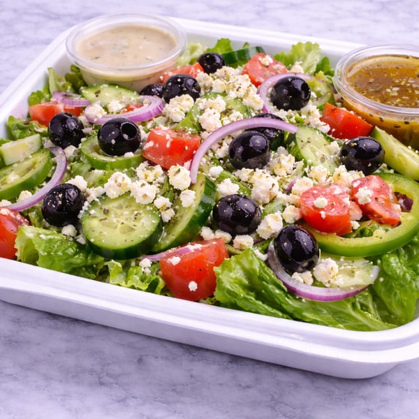 A vibrant Greek salad with lettuce, tomatoes, cucumbers, olives, red onion, and feta cheese.