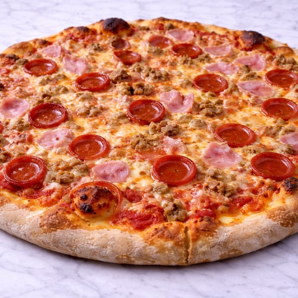 A whole meat lover's pizza with pepperoni, ham, and sausage on a white marble surface.